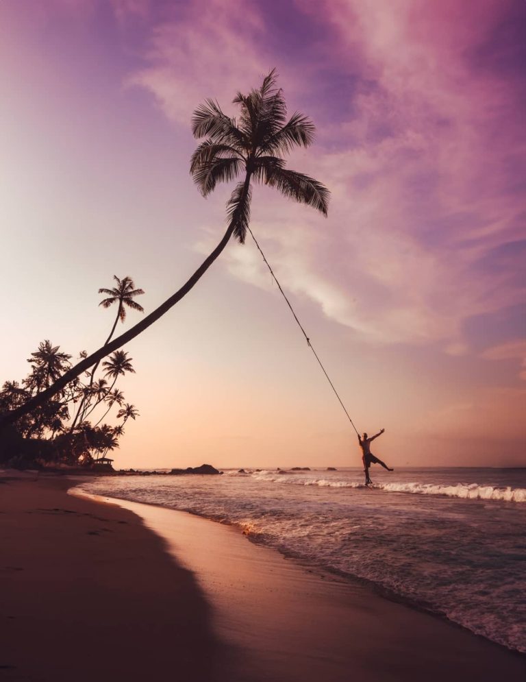 Homem a baloiçar numa palmeira na Praia de Dalawella, no sul do Sri Lanka, ao pôr do sol. Uma visita obrigatória durante um itinerário de 3 semanas no Sri Lanka.