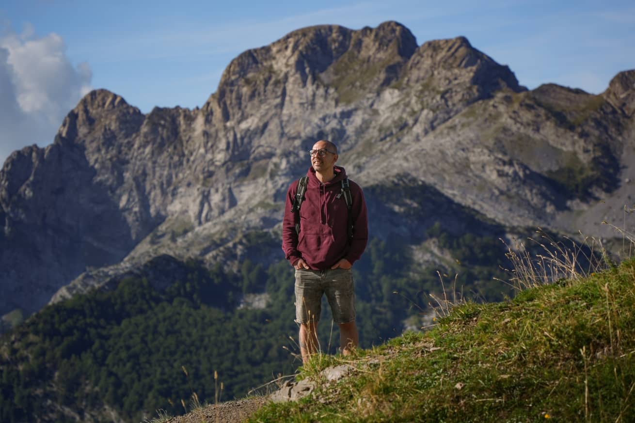 Albania travel blog cover from Chasing Gambozinos, with man smiling with the Albanian Alps in the background