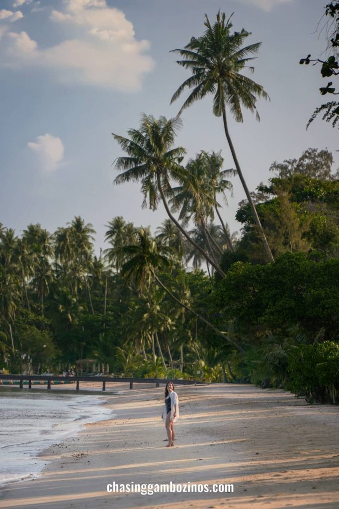 Mulher a caminhar junto à costa da praia de Ao Soun Yai, com belas palmeiras e sem mais ninguém por perto.