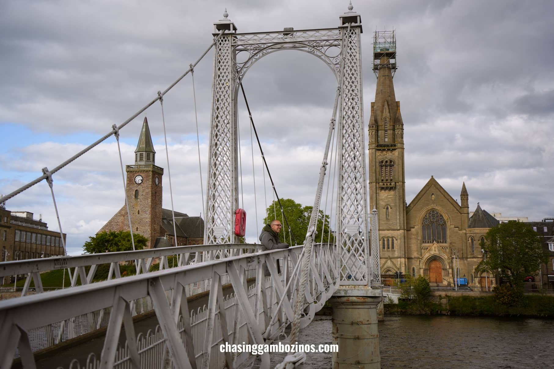 Man standing on the Inverness bridge, with two churches in the background.
