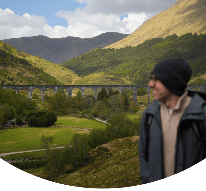 Cover of the Highlands & Isle of Skye Tour from Edinburgh blog from Chasing Gambozinos, featuring a photo of a man at the Glenfinnan Viaduct in Scotland.