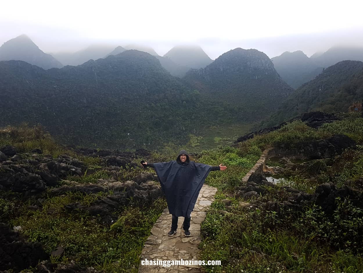 Man with arms wide open wearing a rain poncho during a stop along his Ha Giang loop itinerary.