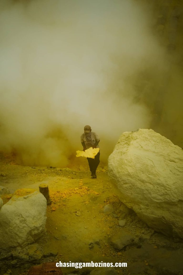 Miner at Mount Ijen holding a piece of sulfur while coming out of a cloud of smoke.